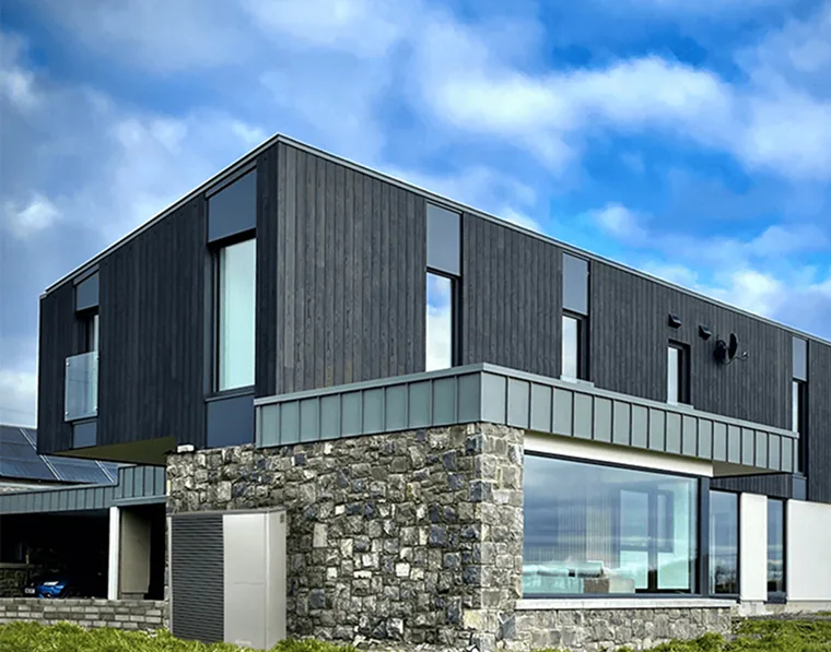 Dark timber-clad Passive House with a stone base and a large corner window